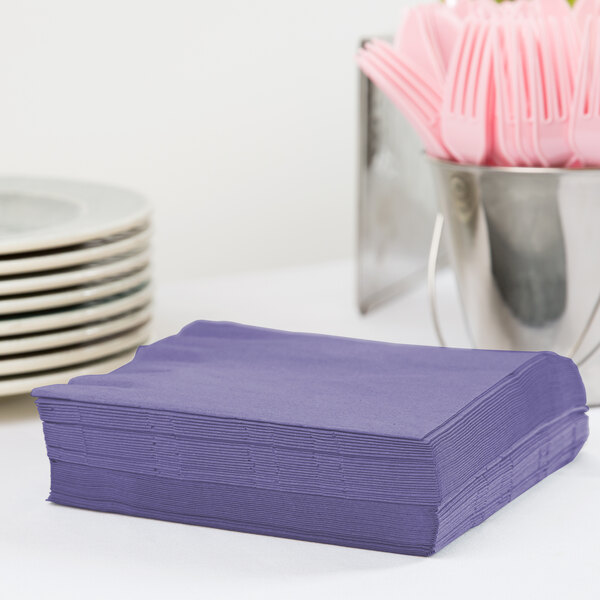 A stack of purple Creative Converting luncheon napkins on a table outdoors.