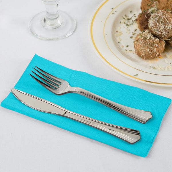 A fork and knife on a Bermuda blue paper dinner napkin next to a plate of food