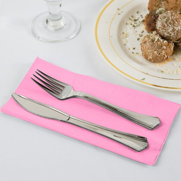 A fork and knife on a pink Creative Converting paper dinner napkin.