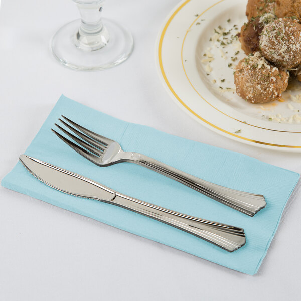 A fork and knife on a blue Creative Converting 2-ply paper dinner napkin on a plate with food.