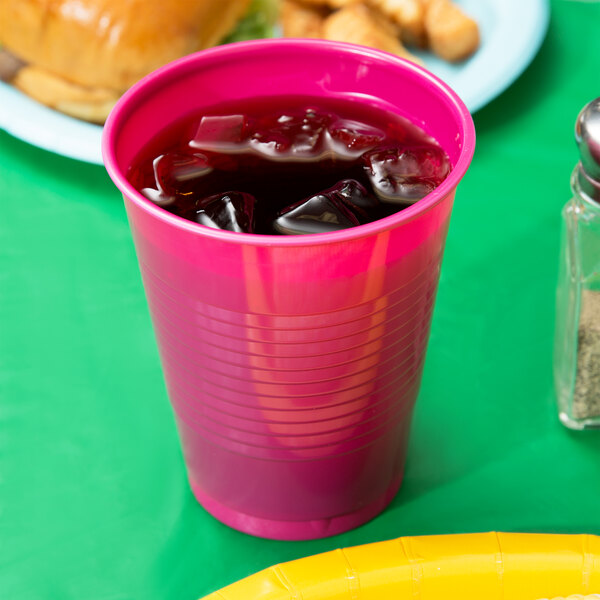 A Creative Converting Hot Magenta Pink Plastic Cup filled with ice on a table.