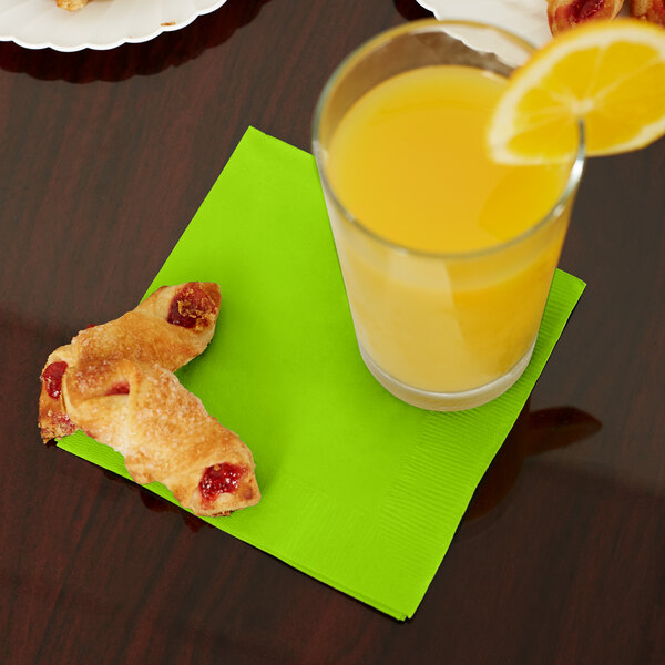 A table with a glass of orange juice with a lime green beverage napkin and pastries.