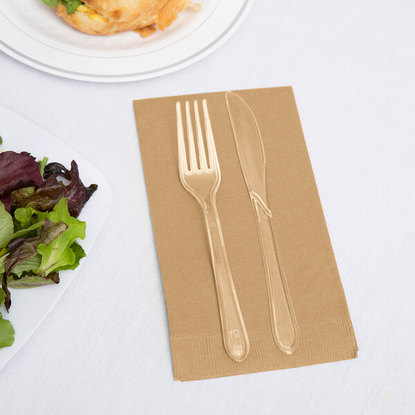 A Creative Converting Glittering Gold guest towel with a fork and knife on it next to a plate of salad.