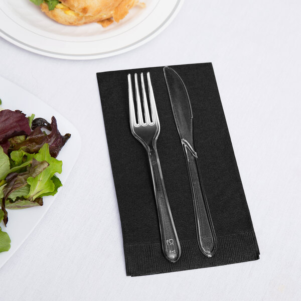 A fork and knife on a black velvet Creative Converting guest towel next to a plate of salad.