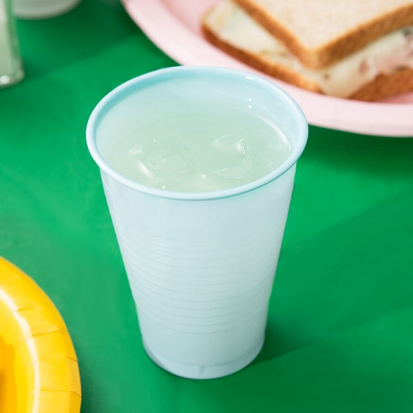 A Creative Converting pastel blue plastic cup filled with a clear liquid and ice on a table with a sandwich.