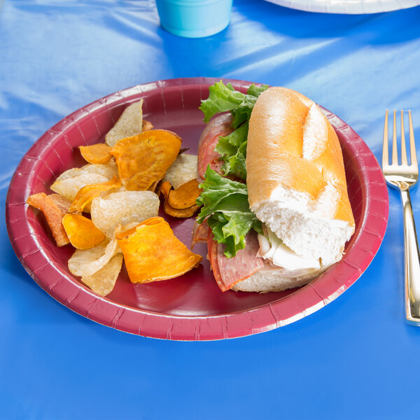 A sandwich on a Creative Converting burgundy paper plate on a table.