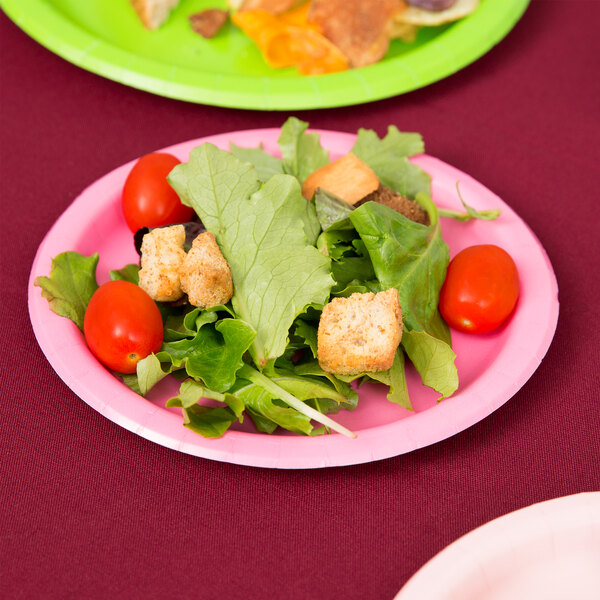 A Creative Converting candy pink paper plate with salad on it on a table.
