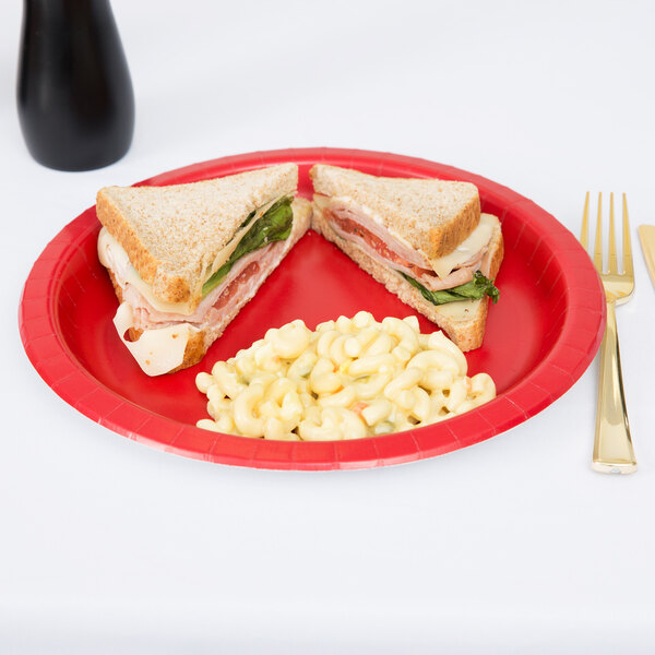 A Classic red paper plate with a sandwich and macaroni and cheese on it.