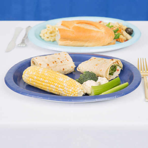 A navy blue oval paper platter with a sandwich, salad, and corn on the table.
