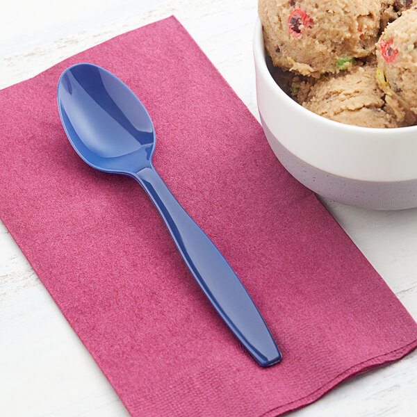 A bowl of ice cream with a navy blue Creative Converting plastic spoon on a table.