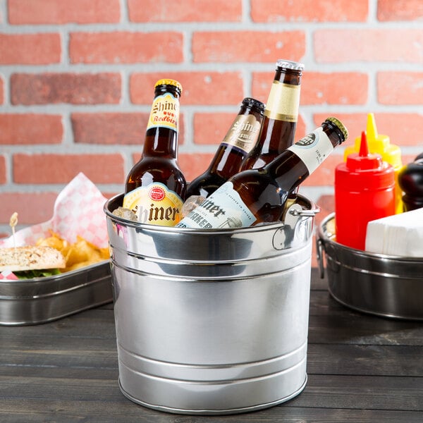 An American Metalcraft stainless steel bucket filled with beer and condiments on a table.