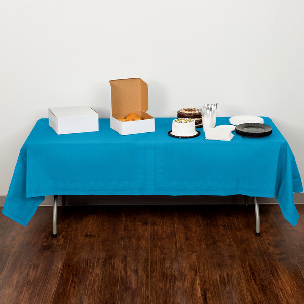 A table with a turquoise blue Creative Converting tablecloth on it with food.