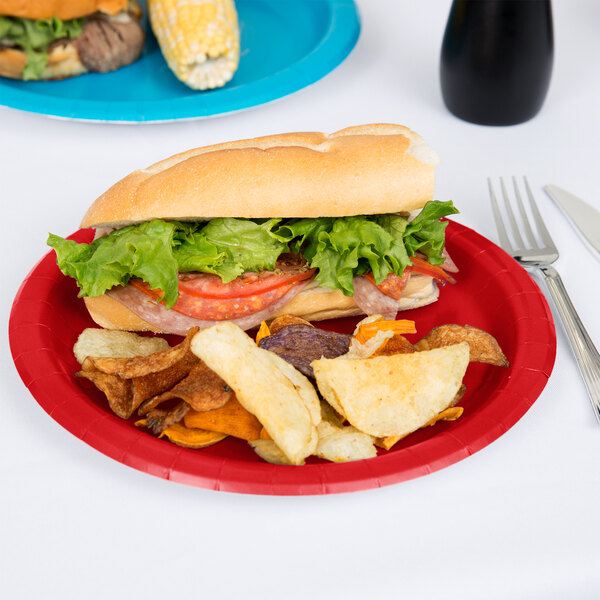 A sandwich with lettuce and tomato on a Classic Red Creative Converting paper plate with potato chips.