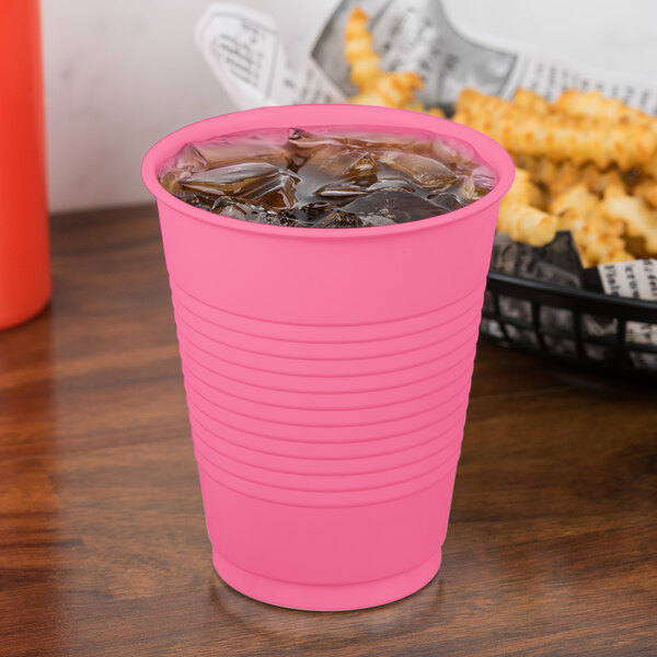 A Creative Converting Candy Pink plastic cup filled with ice on a counter with a drink in it.