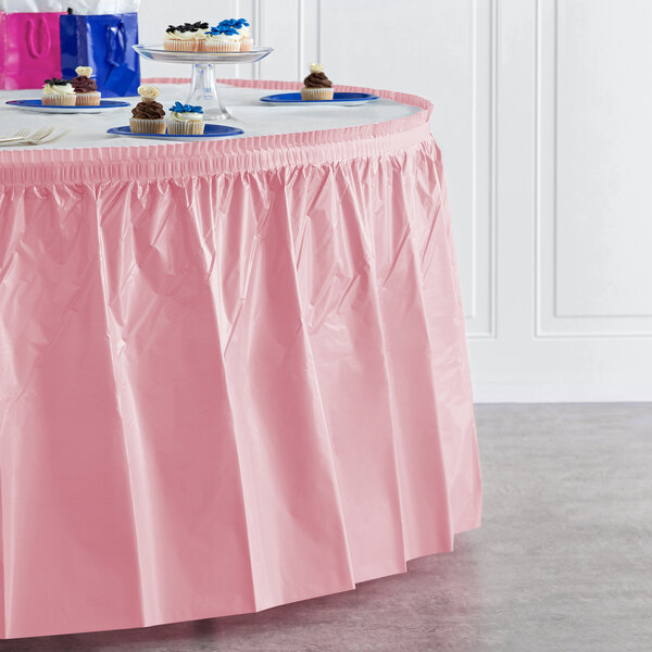 A Classic Pink plastic table skirt on a table with cupcakes.