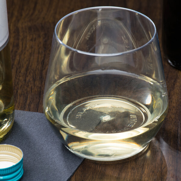 A clear plastic stemless wine goblet filled with white wine next to a bottle of white wine.