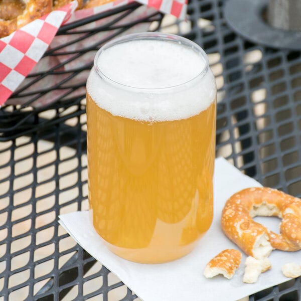 A WNA Comet clear plastic beer can filled with beer next to a pretzel on a table.