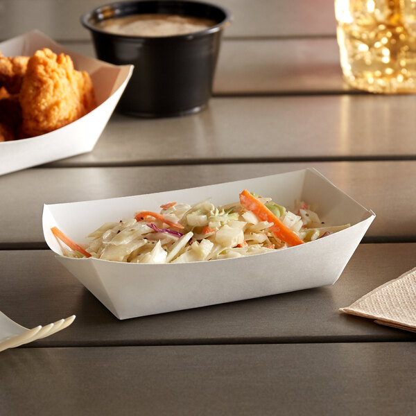 A white paper food tray with coleslaw and chicken wings on it.