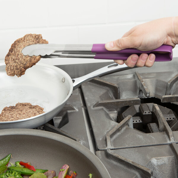 A person using Vollrath Jacob's Pride purple Kool Touch tongs to cook meat in a pan.