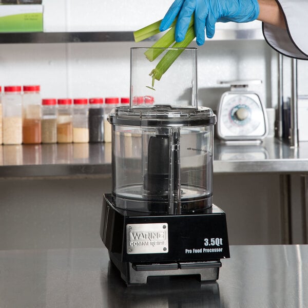 A person in blue gloves putting celery into a Waring food processor.