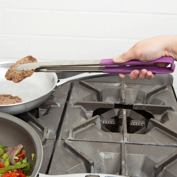 A person using Vollrath Jacob's Pride tongs with purple Kool Touch handles to hold meat in a pan.