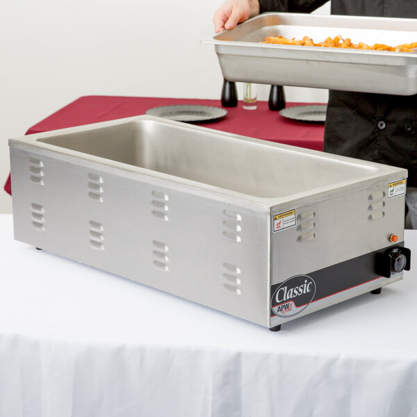 A person using an APW Wyott countertop food warmer to hold a metal pan of food.