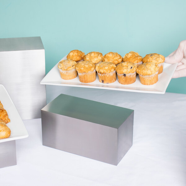 A stainless steel rectangular riser holding a white plate of muffins.