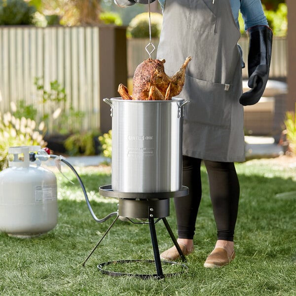 A woman using a Backyard Pro turkey fryer to cook a turkey on a propane tank.