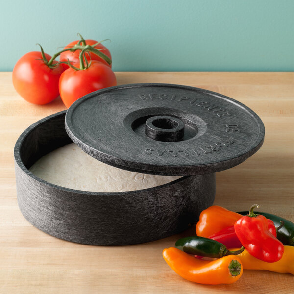 An open round black polyethylene tortilla server on a table with tomatoes and peppers.
