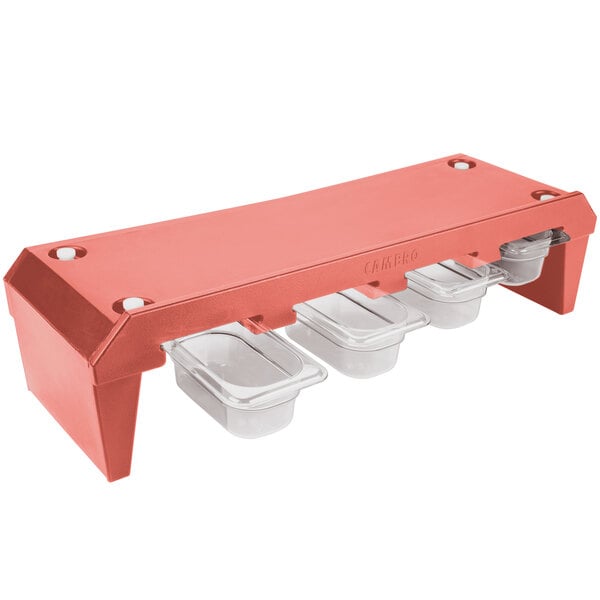 A red plastic condiment rack with four clear plastic containers on top.