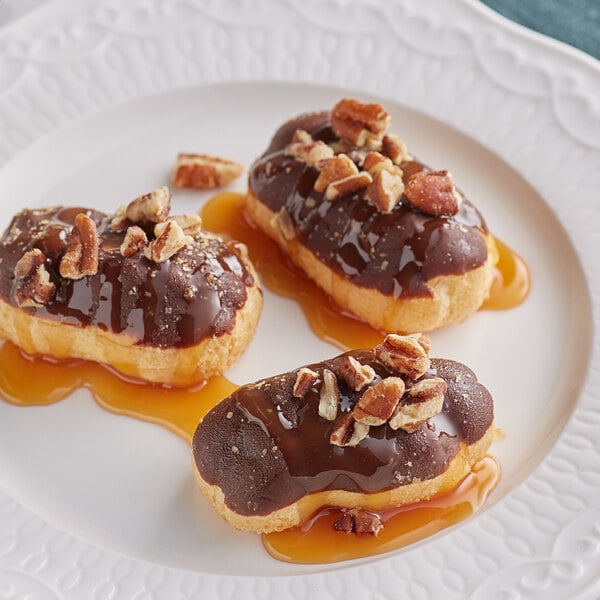 Three chocolate covered donuts drizzled with Ghirardelli Caramel Flavoring Sauce and nuts on a plate.