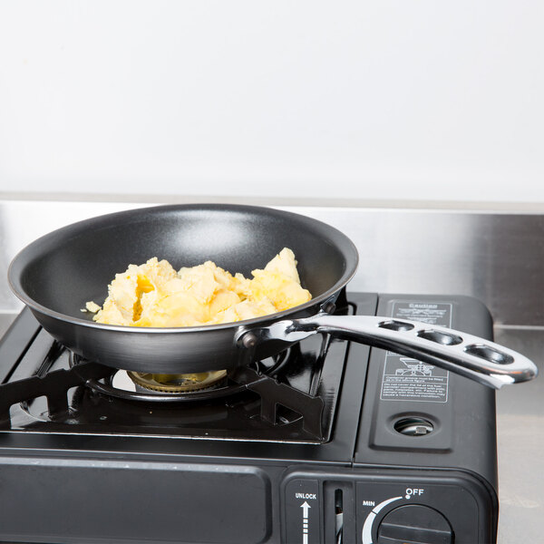 A Vollrath stainless steel non-stick fry pan with eggs cooking in it on a stove.
