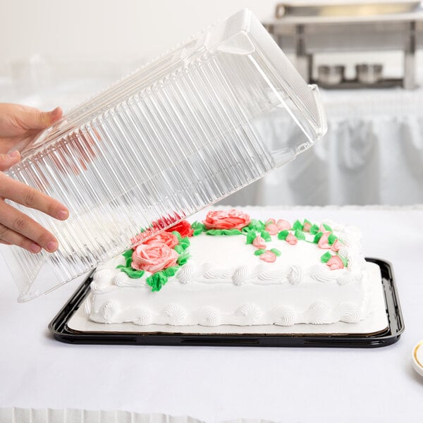A person holding a clear D&W Fine Pack plastic container over a frosted sheet cake on a table.