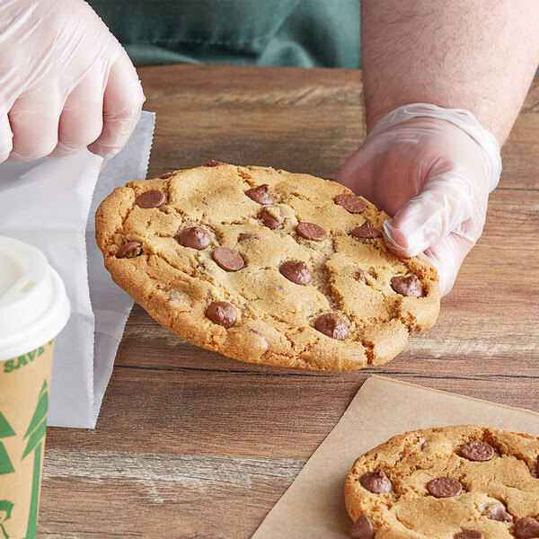 A hand in a glove holding a Ghirardelli milk chocolate chip cookie.