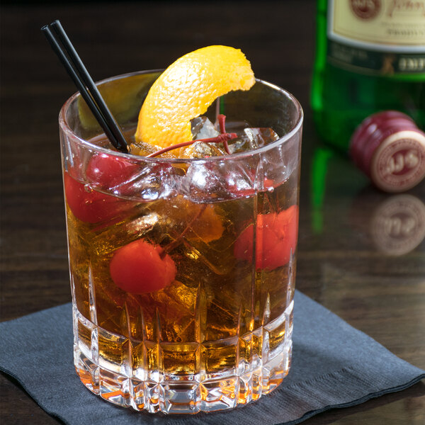 A Spiegelau Perfect Serve Rocks glass filled with ice, whiskey, and cherries with a lemon and orange slice on the table.