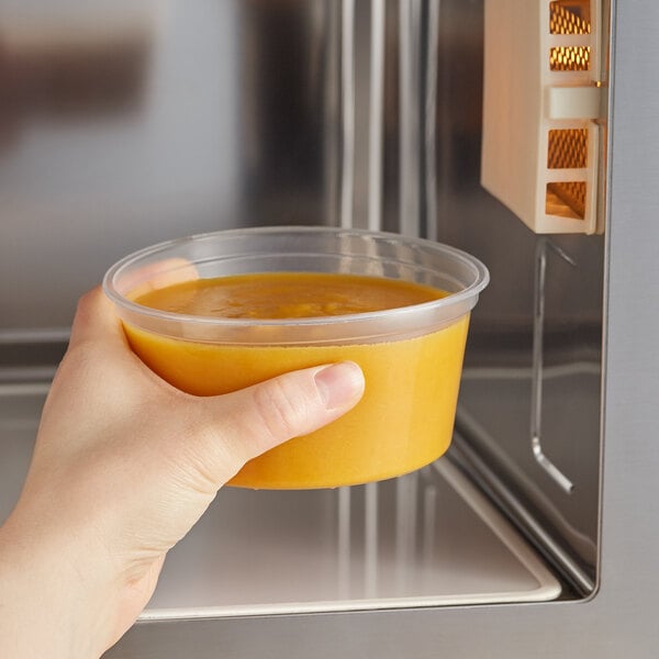 A hand using a Choice translucent plastic deli container to hold food in front of a microwave.