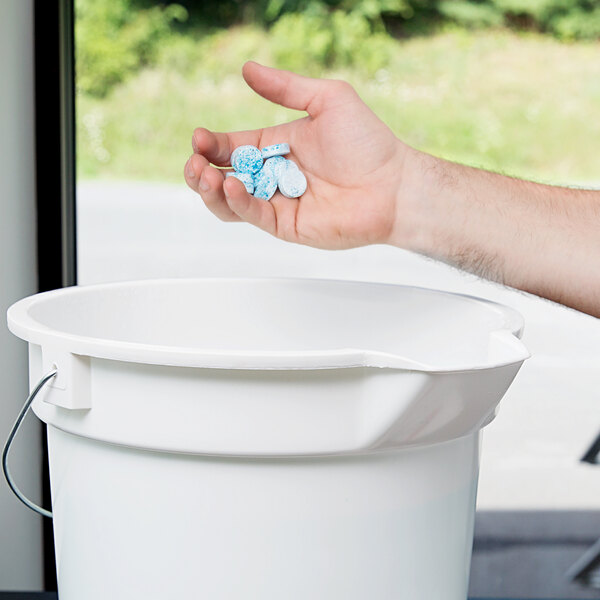 A hand holding a white container of blue Unger The Pill glass cleaner concentrate tablets.
