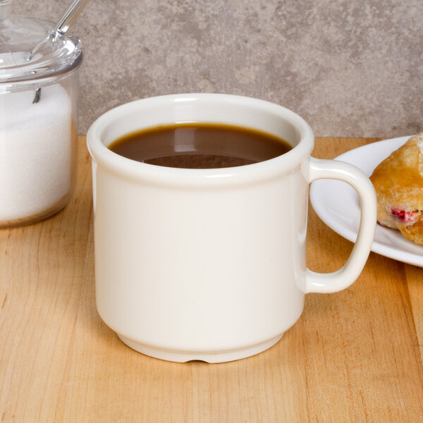 A white GET Diamond Ivory plastic coffee mug filled with brown liquid sitting on a table with a pastry.