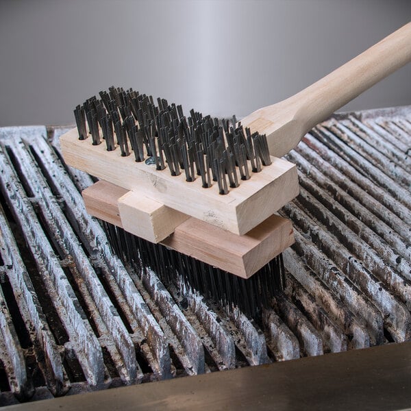 A Carlisle double head grill cleaning brush with metal bristles on a wooden handle.