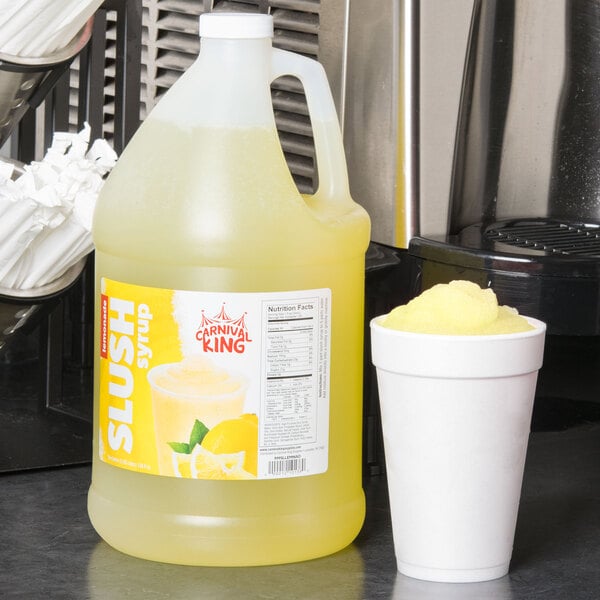 A jug of Carnival King Lemonade Slushy Concentrate next to a cup of slushy.