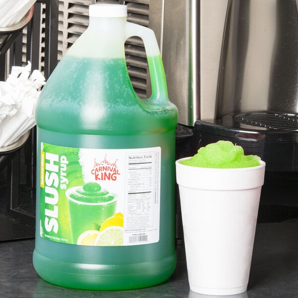 A jug of Carnival King Lemon Lime slushy syrup next to a cup of green slush.