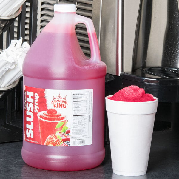 A large jug of Carnival King Fruit Punch Slushy Concentrate next to a cup of fruit punch slushy.