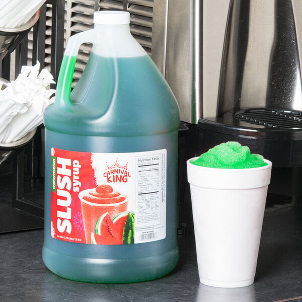 A jug of Carnival King watermelon slushy syrup next to a cup of green slushy.