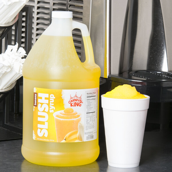 A jug of Carnival King banana slush syrup next to a cup of slushy drink.