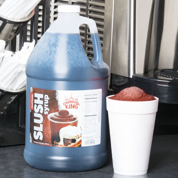 A jug of blue Carnival King Root Beer slushy syrup on a counter next to a white cup with a lid.