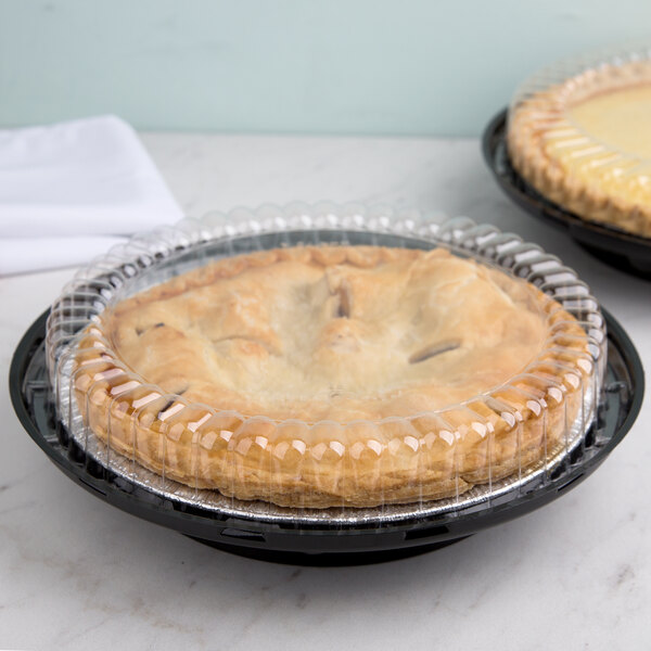 Two pies in D&W Fine Pack plastic containers with clear low dome lids on a table in a bakery display.