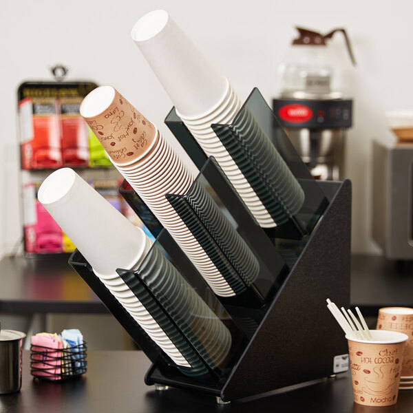 A Vollrath black countertop cup and lid organizer holding a stack of paper cups.