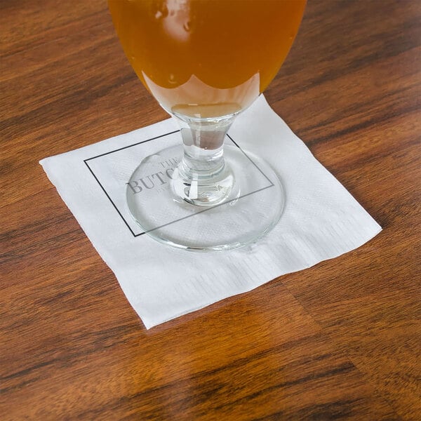 A glass of beer on a white Choice cocktail napkin on a table.