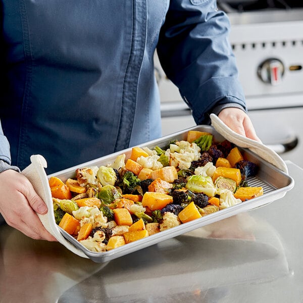 A hand holding a Chicago Metallic aluminized steel jelly roll pan with vegetables.