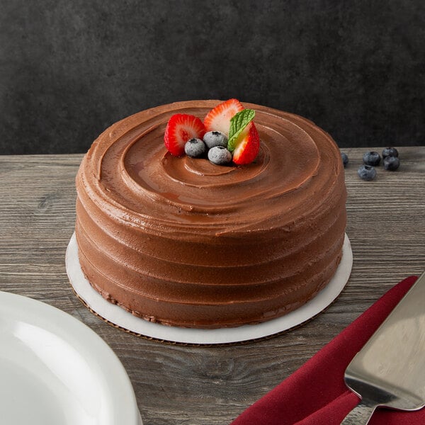 A chocolate cake with strawberries and blueberries on a 9" white corrugated cake circle on a table.